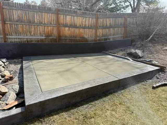 Finished concrete pad with control joints and timber retaining wall in backyard