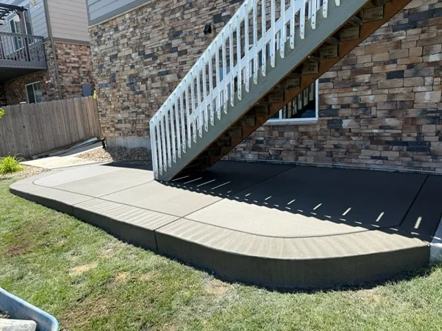 Curved concrete walkway with retaining wall beneath white exterior stairs on brick home