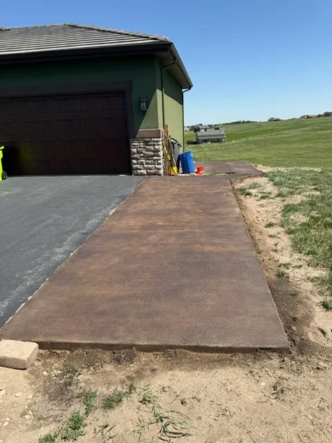 Brown concrete walkway leading to garage with stone veneer accent