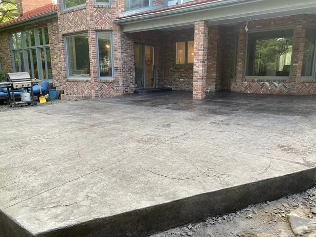 Newly poured concrete patio behind brick home with control joints and proper drainage slope