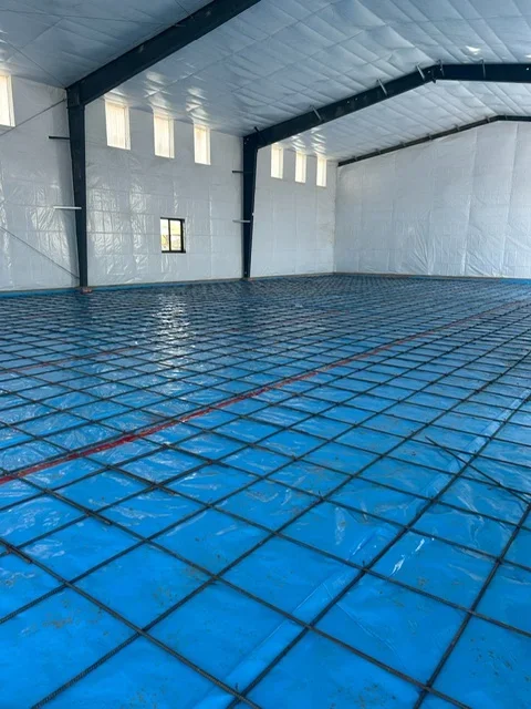 Blue radiant floor heating tubing grid with black supply lines in concrete garage space